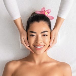 Facial Massage. Attractive asian lady getting face treatment while relaxing in spa